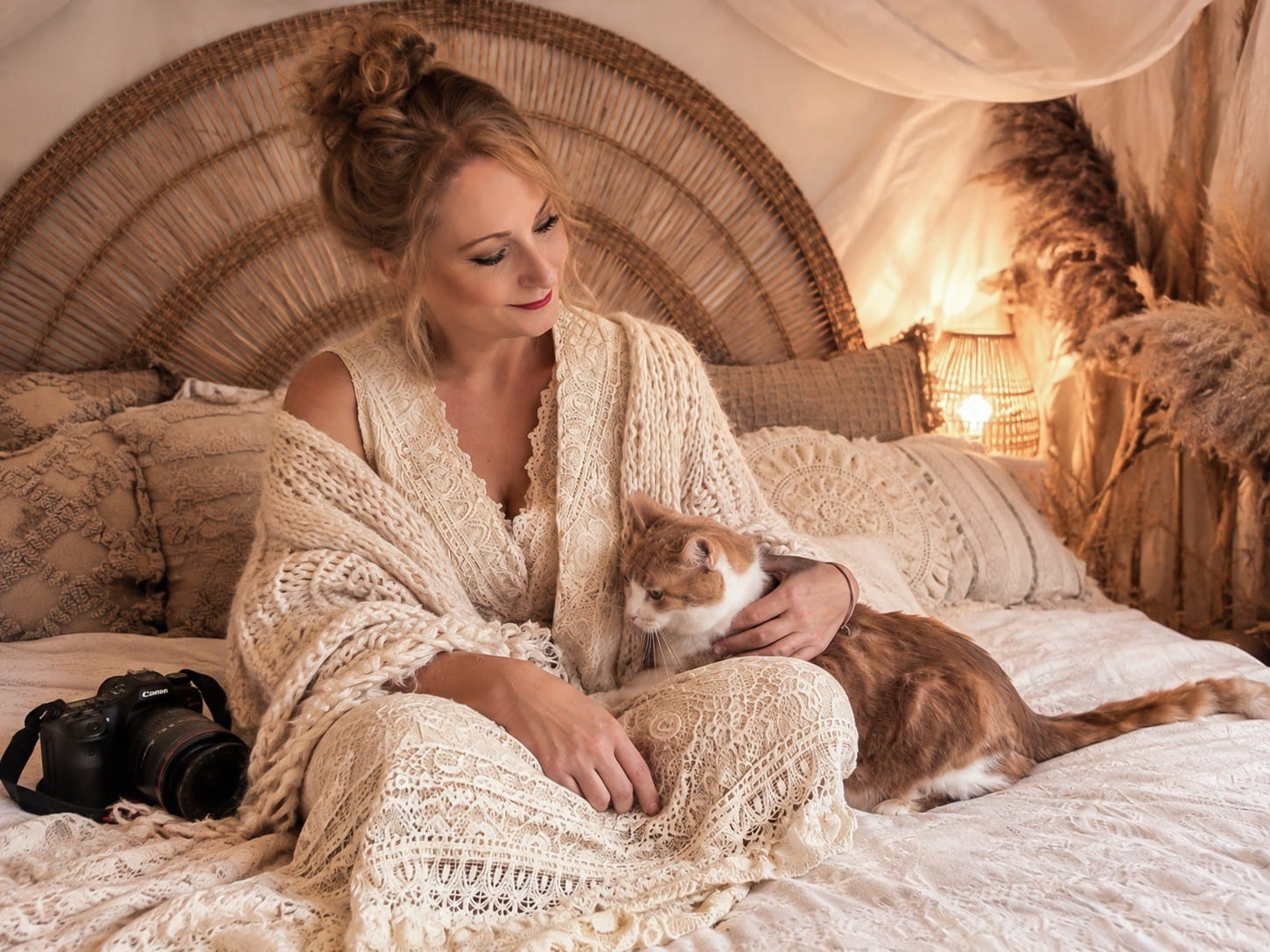 Isabelle Limbach, la photographe, assise sur un lit en dentelle crème, un chat roux et blanc contre elle et son appareil photo posé à côté